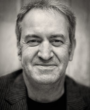 Alan Smyth Episode Two Smiling man with short grey hair, wearing a dark striped blazer against a neutral background.