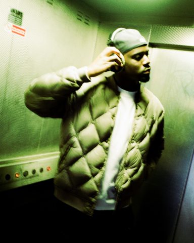 OJKANE Episode One A man wearing a beanie and puffer jacket stands in a dimly lit elevator.